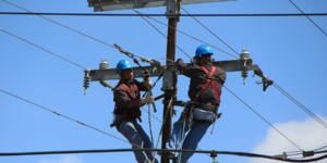 Construction workers on a wire telephone pole.